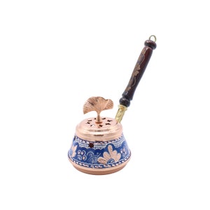 May include: A copper incense burner with a blue and white floral design. The burner has a small, removable lid with a ginkgo leaf design. It comes with a wooden handle.