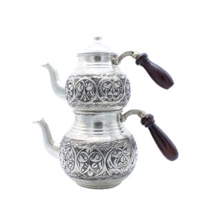 May include: A silver Turkish coffee pot with intricate floral designs and two wooden handles.