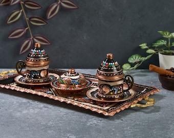 May include: A set of three traditional Turkish coffee cups and saucers with intricate hand-painted designs in black, white, red, and blue on a copper tray with decorative edges.