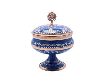 Peut inclure: Un bol à sucre bleu et cuivre avec un couvercle décoratif et un motif floral. Le bol est sur un piédestal.