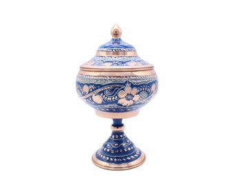 Peut inclure: Un sucrier bleu et cuivre avec des motifs floraux complexes. Le bol a un corps rond avec un couvercle et repose sur un piédestal.