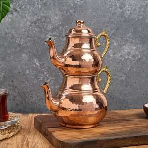 May include: A traditional Turkish tea set made of hammered copper with gold-toned handles. The set consists of two stacked teapots with lids.