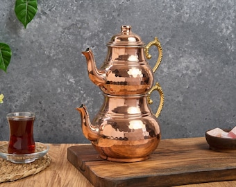 May include: A traditional Turkish tea set made of hammered copper with gold-toned handles. The set consists of two stacked teapots with lids.