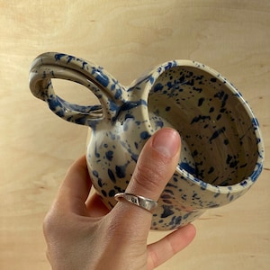 A handmade cup made of beige clay with blue and blue spots, covered with an overgrown glossy glaze