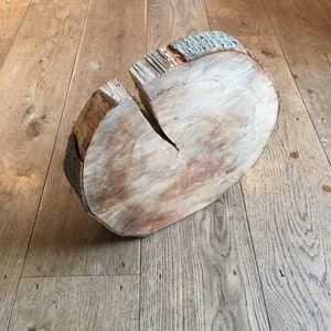 May include: A cross-section of a tree trunk, showcasing the natural wood grain and a visible crack. The bark edge is textured and light green. The wood has a light brown color and is sitting on a wooden floor.