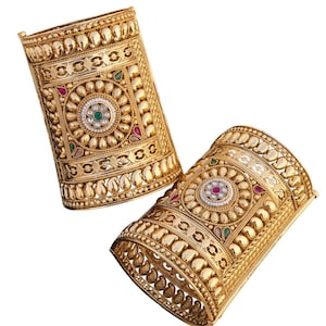 Puede incluir: Un par de brazaletes de metal dorado con diseños intrincados y piedras preciosas de colores. Los brazaletes están decorados con un patrón floral y tienen un borde de cuentas.