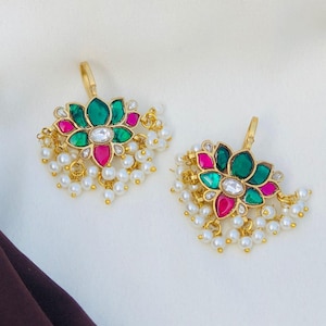 May include: Two gold-toned earrings with a floral design. Each earring features a green and pink flower with a central white stone. Small white pearls dangle from the bottom, and a gold loop is at the top.