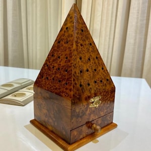May include: A wooden pyramid-shaped incense burner with a drawer and a brass latch. The burner has a brown wood grain finish and is decorated with small holes.
