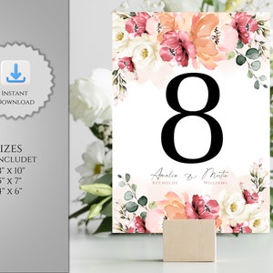 May include: A printable wedding table number card with a floral design in shades of pink, peach, and white. The number 8 is displayed in black font. The text "Amalia & Martin" is printed below the number with the last names "Reynolds" and "Williams" underneath.