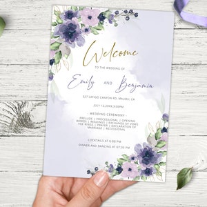 May include: A wedding invitation featuring a watercolour floral design in shades of purple and lavender. The invitation includes the text "Welcome to the wedding of Emily and Benjamin" with the date and time of the wedding ceremony and reception.