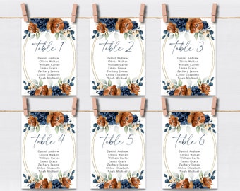 May include: Six table number cards with floral designs in shades of blue, orange, and green. Each card has a gold circle around the table number, which ranges from 1 to 6.