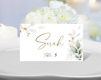 May include: White place card with gold lettering and green watercolor leaves. The name "Sarah" is written in gold script and the text "Table 5" is written in black script.