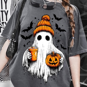 Ghost wearing orange beanie, holding a drink and jack-o’-lantern, with bats and stars around.