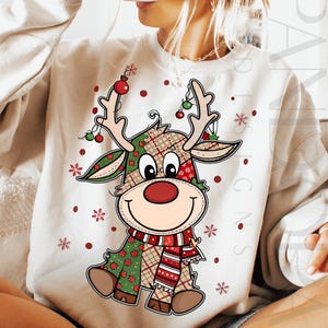 Könnte beinhalten: Cremefarbenes Sweatshirt mit einem Cartoon-Rentier-Design. Das Rentier hat ein Patchworkmuster in Grün, Rot und Braun, eine rote Nase und einen gestreiften Schal. Verziert mit Ornamenten und Schneeflocken, ist es ein festliches Kleidungsstück zum Thema Feiertage.