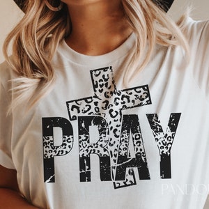 May include: White t-shirt with a black and white leopard print design of a cross and the word "PRAY".