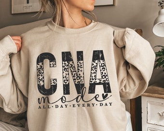 May include: A beige sweatshirt with the text "CNA mode" in black with a leopard print design. The text "ALL DAY EVERY DAY" is printed below the main text.