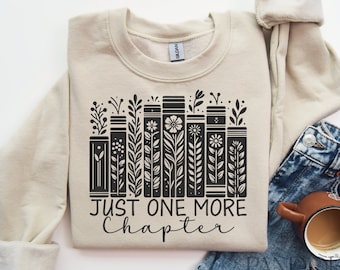 May include: A beige sweatshirt with a black graphic of a stack of books with floral accents and the text "Just One More Chapter".