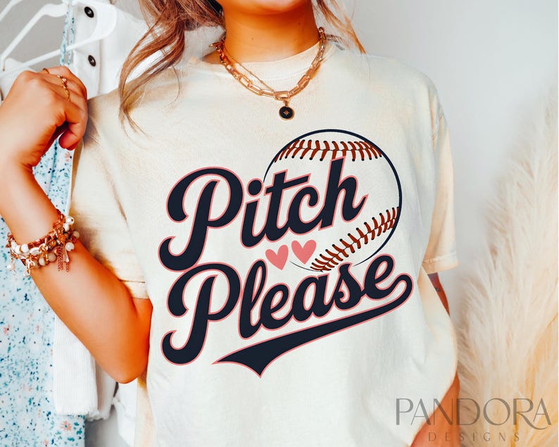 K&ouml;nnte beinhalten: Ein wei&szlig;es T-Shirt mit einem Baseball-Motiv und dem Text "Pitch Please" in Schwarz mit rosa Herzen. Das Shirt wird von einer Person mit einer goldenen Halskette getragen.