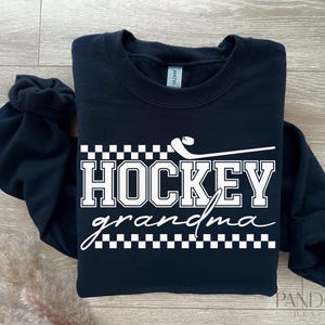 May include: Black sweatshirt with white text that reads "Hockey grandma" with a hockey stick and puck graphic.