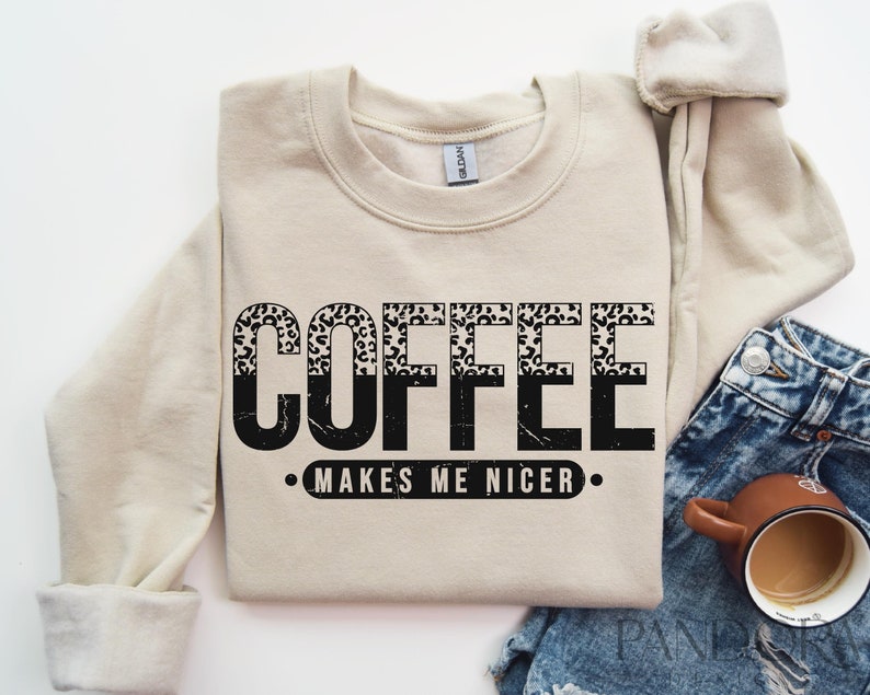 May include: A beige sweatshirt with the text "COFFEE MAKES ME NICER" in black with a leopard print design.