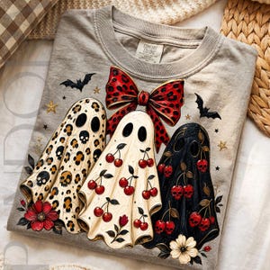 Puede incluir: Una camiseta gris con un gr&aacute;fico de tres fantasmas. Uno tiene estampado de leopardo con calaveras, otro un patr&oacute;n de cerezas y el tercero es negro con calaveras en forma de cereza. Tambi&eacute;n incluye un gran lazo rojo de leopardo, murci&eacute;lagos y estrellas.
