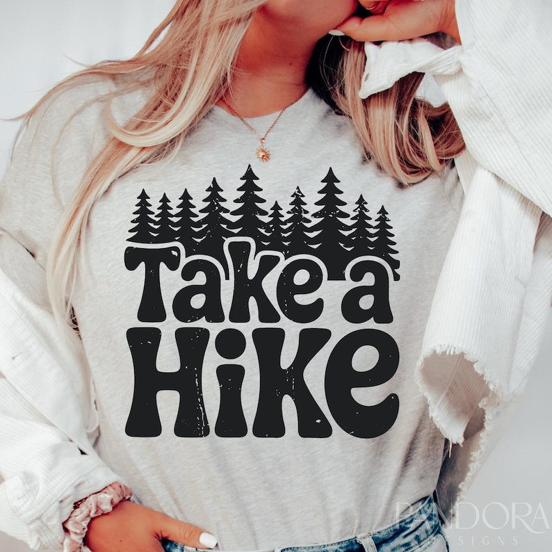 Bold black text saying “Take a Hike” is centered beneath a dense silhouette of pine trees, all in a high-contrast black design on a white background.