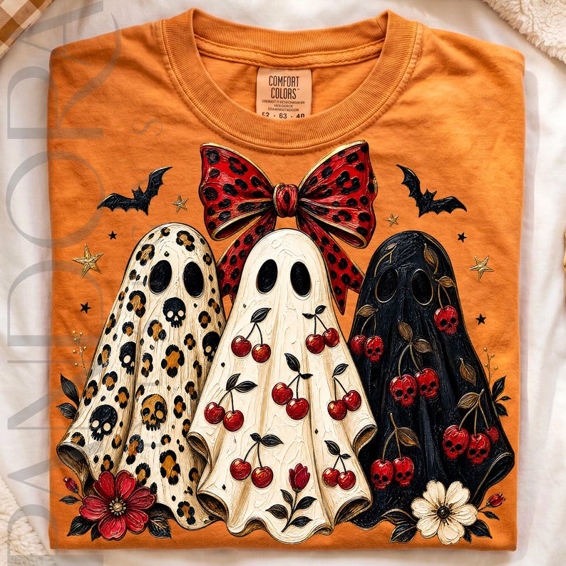 Puede incluir: Una camiseta naranja con un gr&aacute;fico de tres fantasmas. El fantasma izquierdo tiene estampado de leopardo con calaveras, el central tiene un patr&oacute;n de cerezas y el derecho es negro con calaveras en forma de cereza. Un gran lazo rojo sobre ellos.