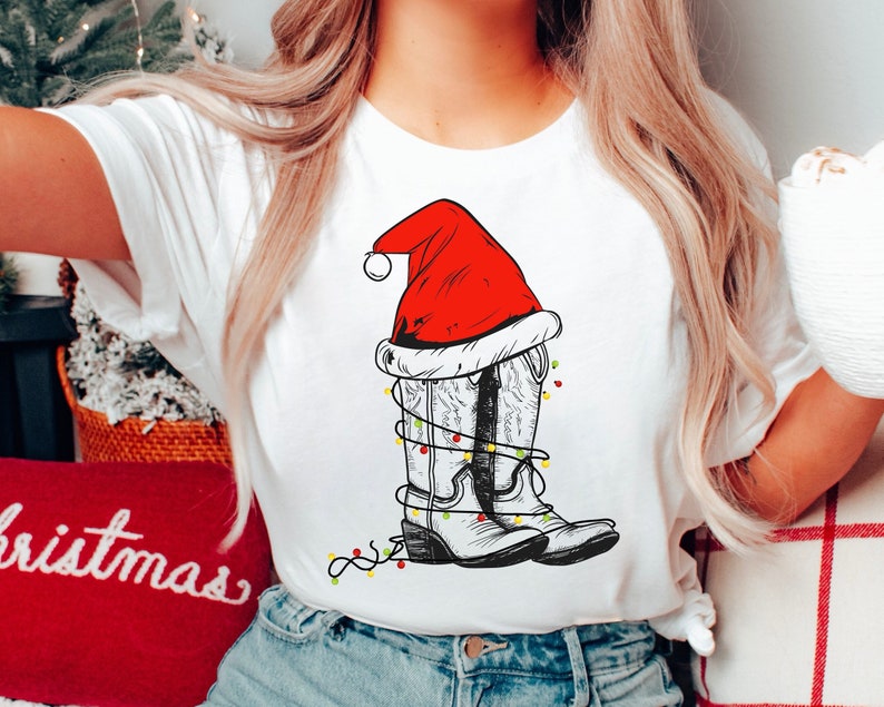 Pu&ograve; includere: Maglietta bianca con un cappello di Babbo Natale rosso e bianco sopra un paio di stivali da cowboy con luci di Natale avvolte intorno.