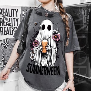 Pu&ograve; includere: T-shirt grigio scuro con un fantasma bianco che tiene in mano una bevanda, circondato da fiori rosa e bianchi. La parola "SUMMERWEEN" &egrave; stampata in nero. La maglietta ha un aspetto vintage e usurato.