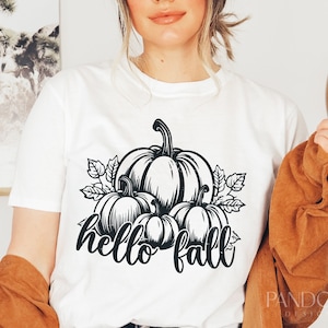 Peut inclure: T-shirt blanc avec un motif noir et blanc de citrouilles et de feuilles. Le texte "hello fall" est &eacute;crit sous les citrouilles.