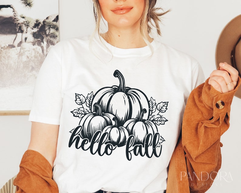 Peut inclure: T-shirt blanc avec un motif noir et blanc de citrouilles et de feuilles. Le texte "hello fall" est &eacute;crit sous les citrouilles.