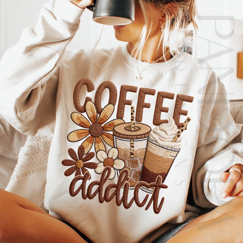 May include: Cream-colored sweatshirt with a brown embroidered design featuring the word "COFFEE" above a floral arrangement and coffee cups. The word "addict" is embroidered below the cups.