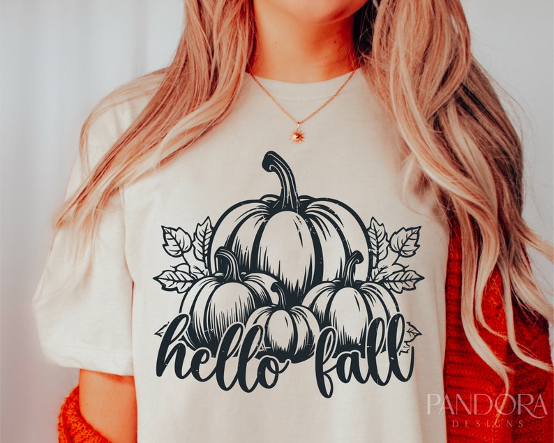 Peut inclure: Un t-shirt blanc avec un motif graphique noir de trois citrouilles et de feuilles. Le texte "hello fall" est &eacute;crit sous les citrouilles.