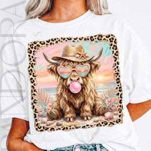 May include: White t-shirt featuring a whimsical illustration of a Highland cow wearing heart-shaped sunglasses, a straw hat, and blowing a bubble. The cow is set against a beach scene with a leopard print border. Seashells and tropical plants are also included.