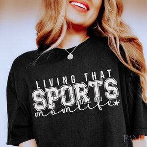 May include: Black t-shirt with white text that reads "Living that Sports Mom Life" with a star.