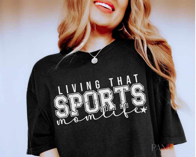 May include: Black t-shirt with white text that reads "Living that Sports Mom Life" with a star.