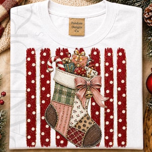 May include: A white t-shirt featuring a graphic of a patchwork Christmas stocking filled with gifts and a candy cane. The stocking is decorated with a large pink bow and bell, set against a background of vertical red stripes with white polka dots.
