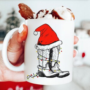 Pu&ograve; includere: Tazza in ceramica bianca con un'illustrazione disegnata a mano di stivali da cowboy che indossano un cappello di Babbo Natale e luci di Natale.