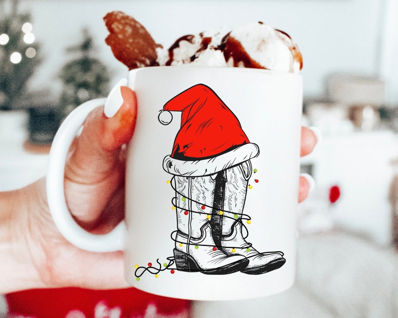 Pu&ograve; includere: Tazza in ceramica bianca con un'illustrazione disegnata a mano di stivali da cowboy che indossano un cappello di Babbo Natale e luci di Natale.