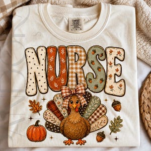 May include: A cream-colored t-shirt featuring the word NURSE in large, patterned letters with polka dots, floral, and gingham designs. Below, a cartoon turkey with a gingham bow wears a festive outfit, surrounded by a pumpkin, acorns, and leaves.