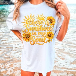 May include: White t-shirt with a yellow and orange floral design featuring sunflowers and the text "there is sunshine in my soul". The shirt has short sleeves and a crew neck.