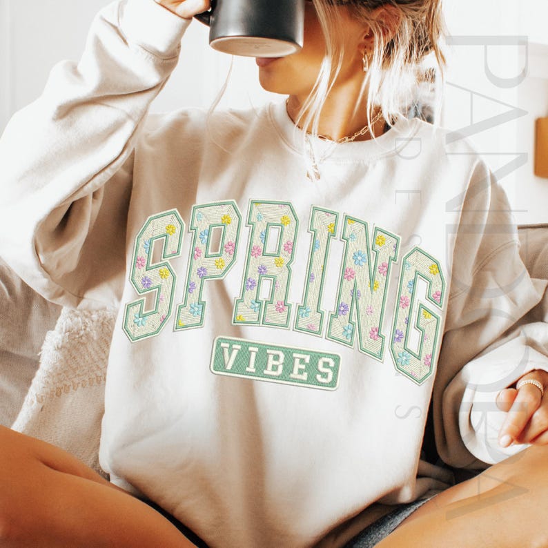 May include: Cream-colored sweatshirt with the words "SPRING VIBES" in a floral design. The letters are outlined in light green, with a floral pattern inside. The word "VIBES" is in a rectangular box below the word "SPRING".