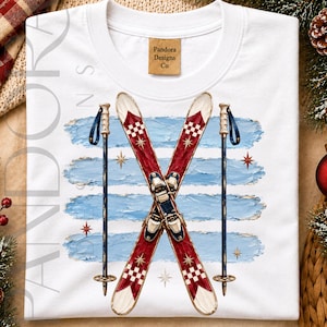 May include: A white t-shirt featuring a graphic of two crossed red and white checkered skis and two blue ski poles. The design is set against four horizontal light blue textured brushstrokes with small gold star accents and a neck label reading Pandora Designs Co.