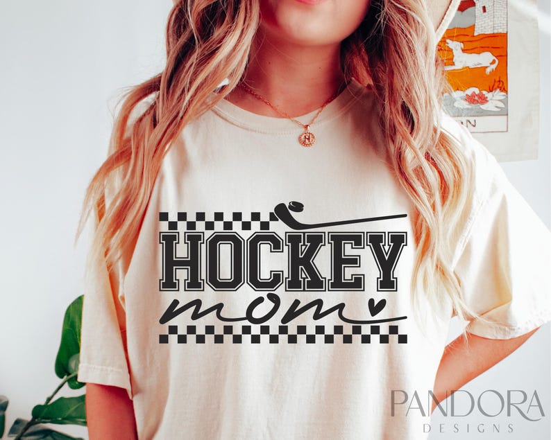 May include: A white t-shirt with a black graphic that says "HOCKEY mom" with a hockey stick and a heart. The graphic is surrounded by a black and white chequered pattern.