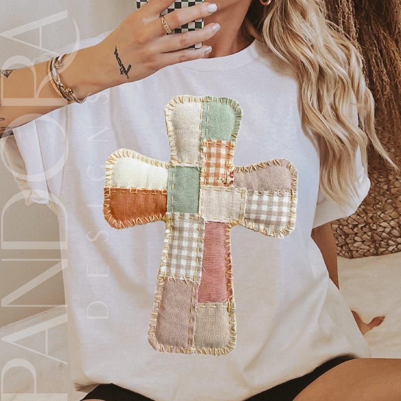 Peut inclure: T-shirt blanc avec un motif de croix en patchwork dans des tons orange, vert et rose. La croix est compos&eacute;e de diff&eacute;rents motifs et textures de tissu. Le t-shirt porte l'inscription "PANDORA DESIGNS".