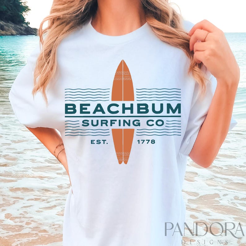 May include: White t-shirt with a surfboard graphic. The design includes the text "BEACHBUM SURFING CO." in teal, with a brown surfboard illustration. The shirt also features "EST. 1778".