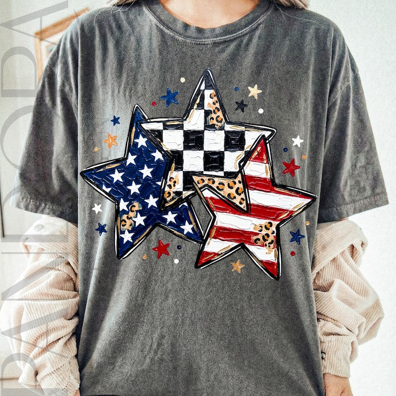 May include: A gray t-shirt featuring three star designs. One star has a blue background with white stars, another has a black and white checkered pattern, and the third has red and white stripes. The stars have leopard print accents.
