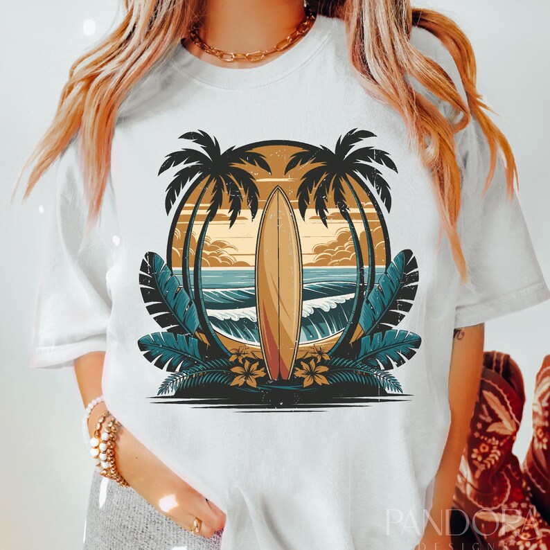 May include: White t-shirt with a graphic of a surfboard in front of a sunset with palm trees on either side.
