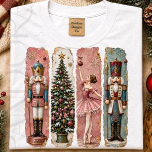 May include: A white t-shirt featuring a graphic print of four vertical panels. The panels display a nutcracker in a crown, a decorated Christmas tree, a ballerina in a pink tutu, and a nutcracker in a tall hat. The brand label reads Pandora Designs Co.