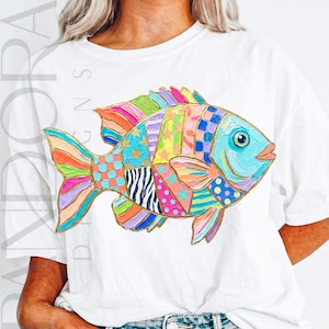 May include: White t-shirt featuring a colorful, patchwork-style fish design. The fish has a blue eye and is composed of various patterns and colors, including stripes, stars, and polka dots. The design is outlined in gold.